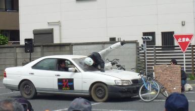 自転車に乗車したスタントマンが、車に跳ね飛ばされている写真